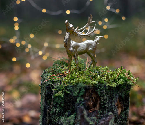 Christmas golden deer toy on the tree stump in forest close up. . Winter holiday greeting card close up © mariarom