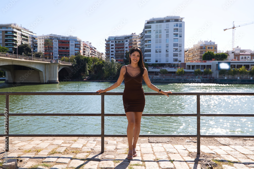 young and beautiful woman from south america and dressed in short dress is on vacation in seville. In the background the river. The woman smiles and makes different expressions. Travel and vacation.