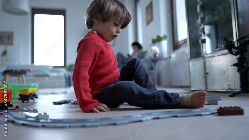 Child playing with railroad train toy at modern home living room floor. Little boy plays by himself with gift toys Child playing with railroad train toy at modern home living room floor. Little boy plays by himself with gift toys