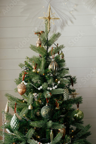 Stylish christmas tree with vintage baubles and golden lights. Modern decorated christmas tree with vintage ornaments in festive scandinavian room. Winter holidays preparation