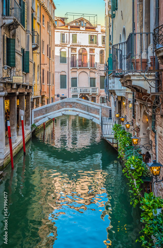 Narrow canal with small bridge and romantic lights on beautiful Venetian buildings in city center of Venice, Italy.  © Nancy Pauwels