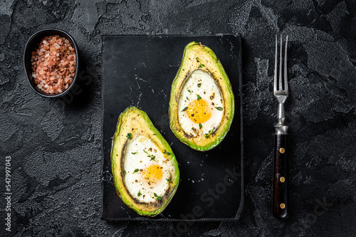 Eggs baked in avocado with herbs and spices. Black background. Top view