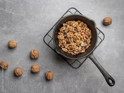 Roasted walnuts in black pan and walnut shells against concrete background. Overhead shot with copy space.