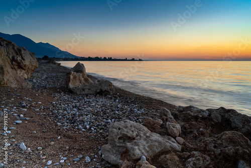 peaceful sunset over the ocean with silhouette of mountains and pebble beach iwth rock boulders in the foreground