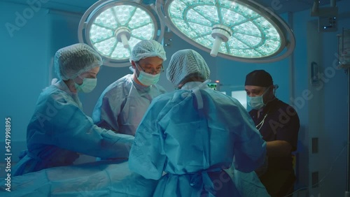 Four medical surgeons are in a room filled with different medical equipment working on a patient and standing around him.