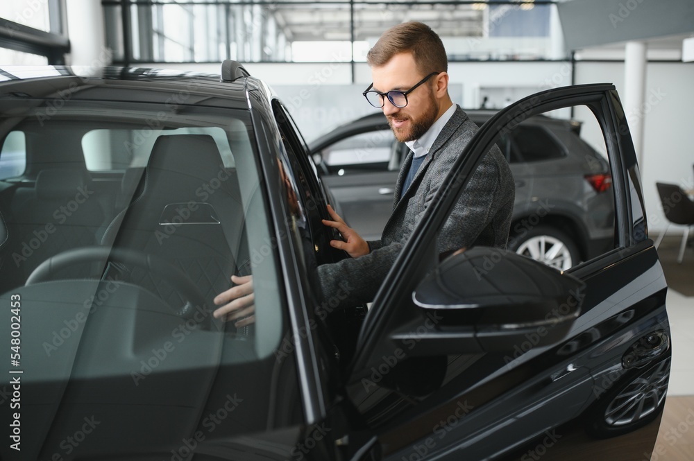 Man adult customer male buyer client wears classic suit white shirt chooses auto wants to buy new automobile touch check car in showroom vehicle salon dealership store motor show indoor. Man adult customer male buyer client wears classic suit white shirt chooses auto wants to buy new automobile touch check car in showroom vehicle salon dealership store motor show indoor.