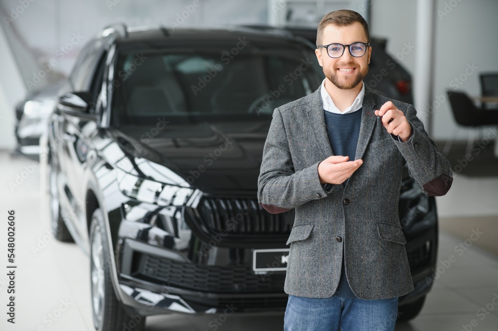 Portrait of a handsome salesman in the suit standing near the car in the showroom Portrait of a handsome salesman in the suit standing near the car in the showroom