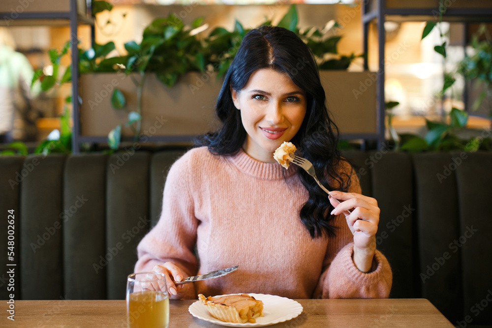 Young woman with curly hair in a pink sweater eating an apple pie at a table in a cafe. Young woman with curly hair in a pink sweater eating an apple pie at a table in a cafe.