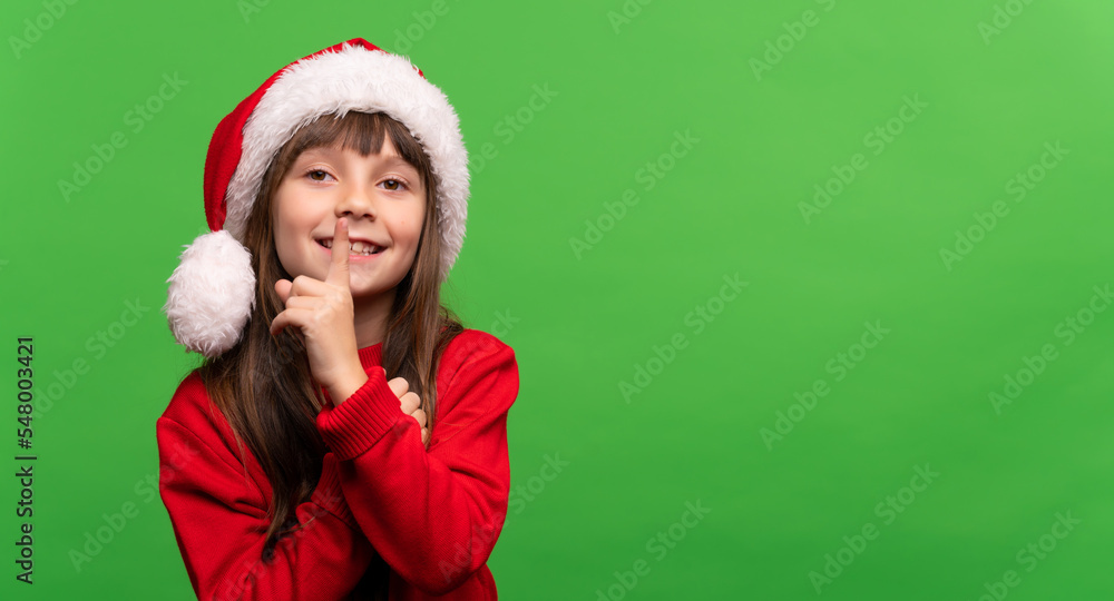 Don't give a surprise. Cute smiling little Santa girl in a hat put her finger to her lips. Silence sign. New Year and Christmas concept. Time to give gifts Don't give a surprise. Cute smiling little Santa girl in a hat put her finger to her lips. Silence sign. New Year and Christmas concept. Time to give gifts