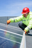 operaio con caschetto protettivo rosso , tuta specialistica e occhiali tecnici lavora su un impianto fotovoltaico istallato sul tetto di un edificio