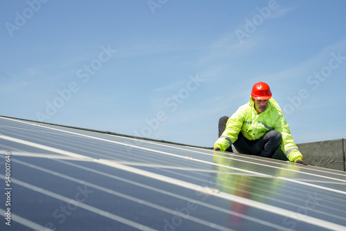 operaio con caschetto protettivo rosso , tuta specialistica e occhiali tecnici lavora su un impianto fotovoltaico istallato sul tetto di un edificio photo