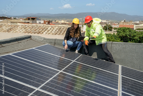 un ingegnere con l'operaio controllano la posa in opera dei pannelli fotovoltaici nel tetto di un edificio photo