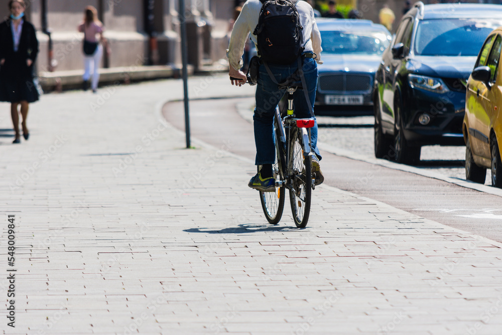 Fototapeta premium Unrecognizable man riding a bike in city with blurred people and cars in background in hard sunlight