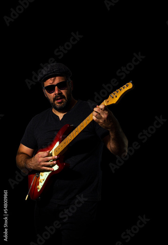 Man playing electric guitar wearing a flat cap and sunglasses. © Stefano