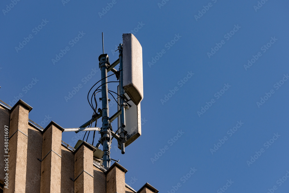 Close up to a 5G antenna with dish mounted high on the roof of a modern construction Close up to a 5G antenna with dish mounted high on the roof of a modern construction