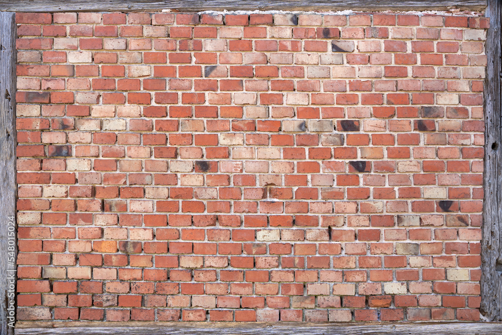 Obraz premium Alte rote Backsteinwand eingerahmt von verwitterten grauen Holzbalken