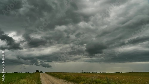 A timelapse storm over a field and a dirt road. Gray rain clouds are raging over a wheat field. The hurricane threatens to destroy crops. Time lapse cloud movement