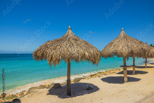 View of sun beds and umbrellas on sandy beach on turquoise water surface and blue sky background. Aruba. 