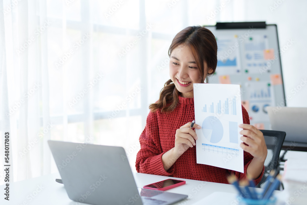 Beautiful young Asian businesswoman is video chatting with customer using laptop in office and is negotiating and explaining the details of the document with a smiling and happy expression. Beautiful young Asian businesswoman is video chatting with customer using laptop in office and is negotiating and explaining the details of the document with a smiling and happy expression.