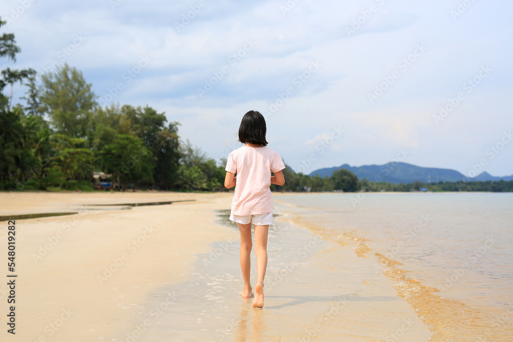 Back view of Asian girl child walking alone on tropical sand beach.