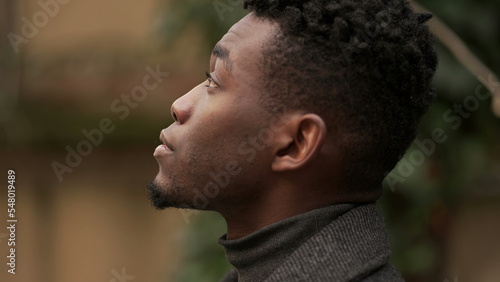 Pensive black African man standing outdoors thinking, looking up at sky in contemplation