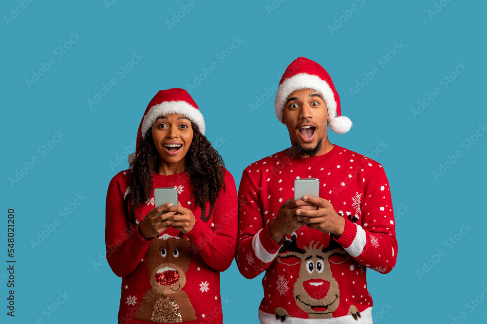 Amazed african american couple using smartphones on blue Amazed african american couple using smartphones on blue