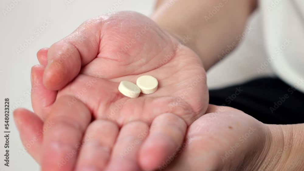 Wrinkled palms of mature woman with painkiller headache pills on blurred background. Female person shows effective medication to fight pain closeup Wrinkled palms of mature woman with painkiller headache pills on blurred background. Female person shows effective medication to fight pain closeup
