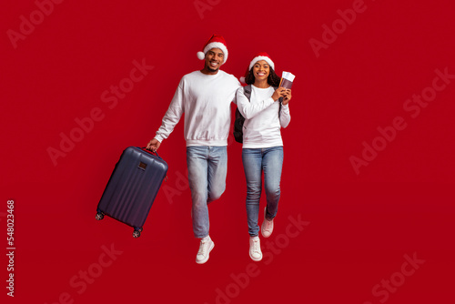 Happy black couple in Santa hats holding passport, tickets