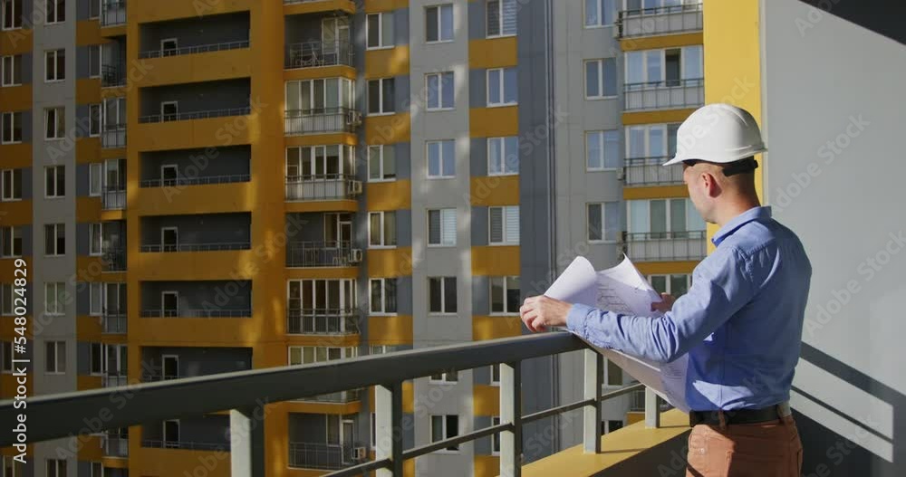 Architect looks around apartment complex and examines drawings. Adult designer controls building process of flats block at bright sunlight Architect looks around apartment complex and examines drawings. Adult designer controls building process of flats block at bright sunlight