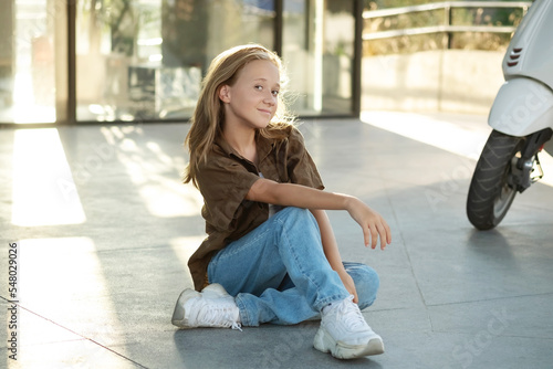 Portrait of teenage girl sitting on floor, urban street, sunlight