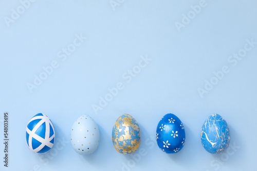 Frame of Easter golden decorated eggs in nest on blue background for web banner. Minimal easter concept. Happy Easter card with copy space for text. Top view, flatlay