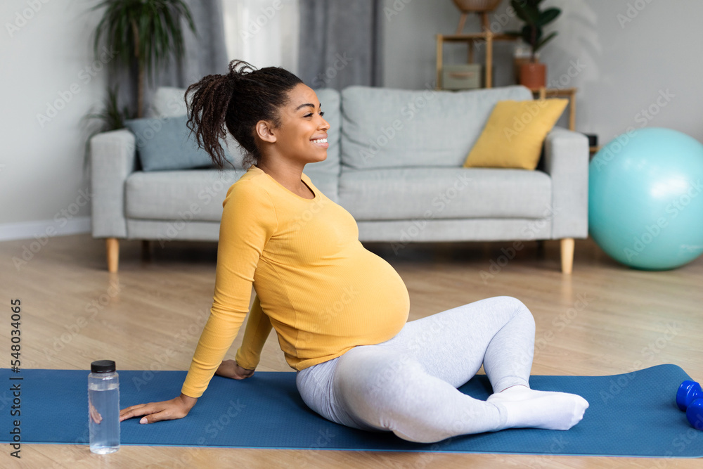 Glad young black pregnant female with big belly doing exercises, practicing yoga, rest and relax after sports workout Glad young black pregnant female with big belly doing exercises, practicing yoga, rest and relax after sports workout