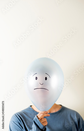 Woman dressed in blue with a balloon on her head with a sad face drawn on her head.
