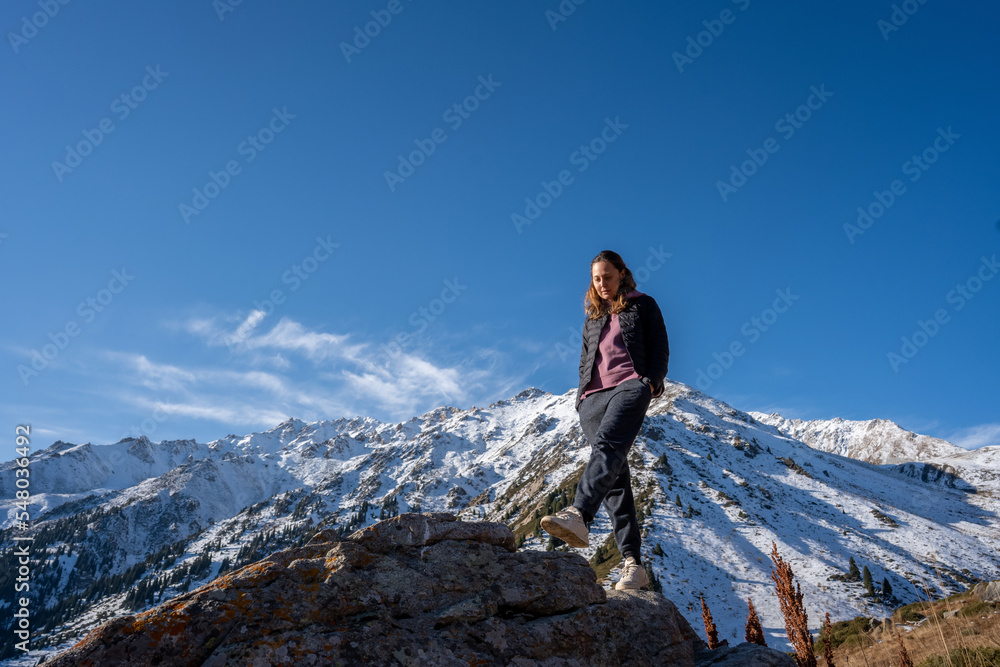 Serene woman walking on a rock, strolling surrounded by snowy mountains on a sunny day. Upward against the sky.