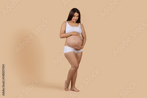 Full Length Shot Of Young Pregnant Woman In Underwear Embracing Belly