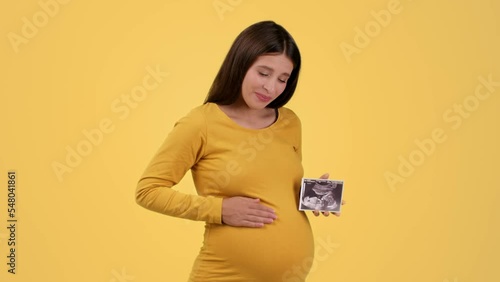 Young happy pregnant woman holding sonography picture of her baby and smiling, caressing and tickling her big belly photo