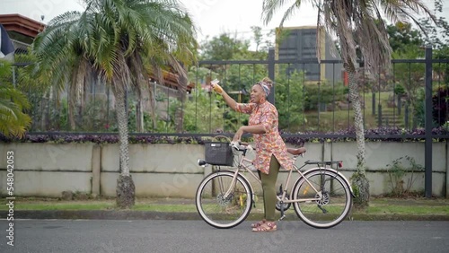 Imagen en video de una mujer afro caribeña de cuerpo completo con ropa colorida vendiendo en la calle sus productos en una bicicleta muy feliz photo