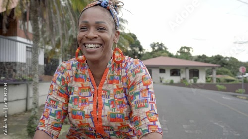 Mujer afro caribeña con una gran sonrisa montada en una bicicleta ofreciendo productos para la venta en la calle con ropa muy colorida photo
