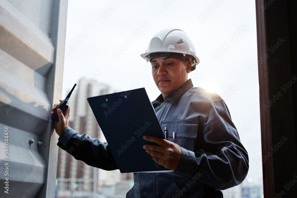 Backlit portrait of female worker wearing hardhat standing in container door at shipping docks Backlit portrait of female worker wearing hardhat standing in container door at shipping docks