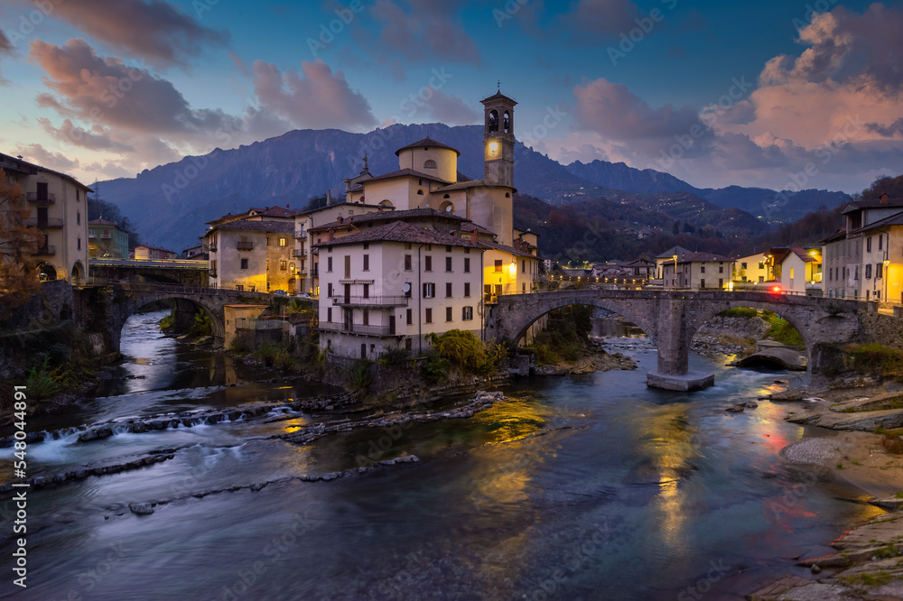 Aerial villagescape - old church and crossing rivers with mountains backdrop, San Giovanni Bianco Village, Valbrembana, Bergamo, Lombardy, Italy