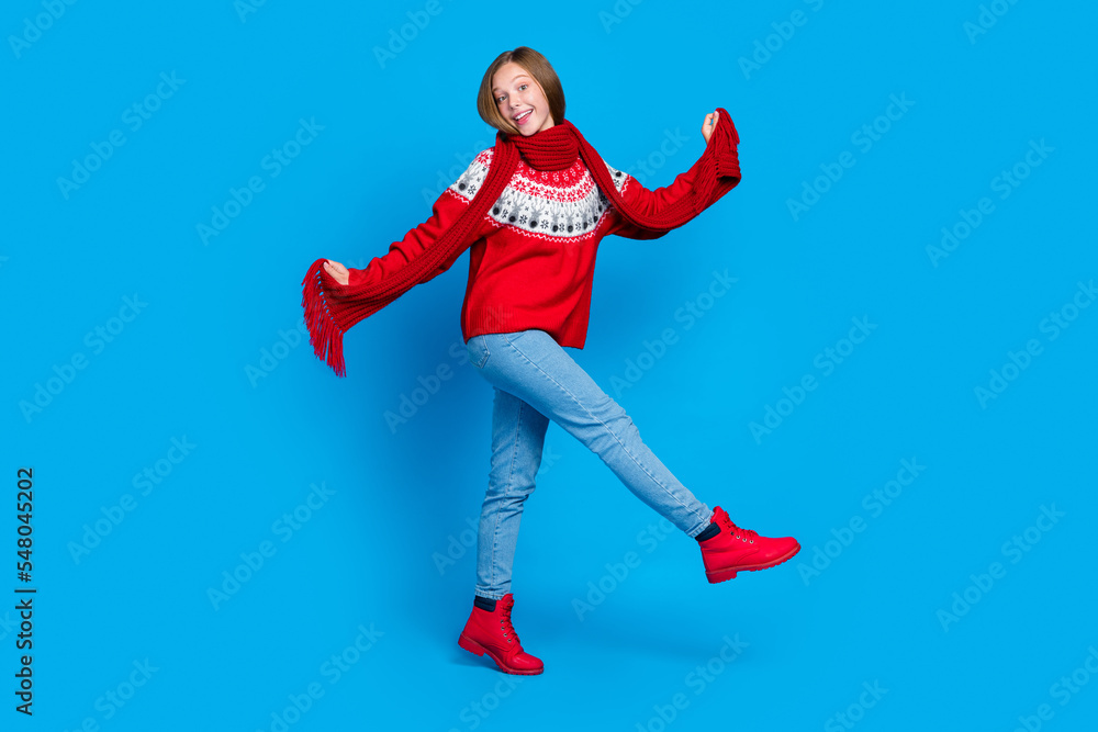 Full length photo of cool charming school girl dressed red x-mas ornament pullover walking having fun isolated blue color background Full length photo of cool charming school girl dressed red x-mas ornament pullover walking having fun isolated blue color background