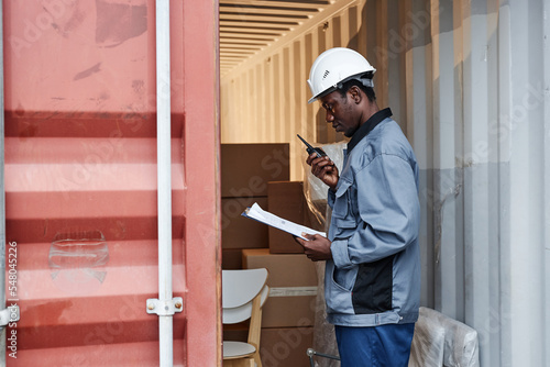 Side view portrait of male worker wearing hardhat while checking containers at shipping dock, copy space