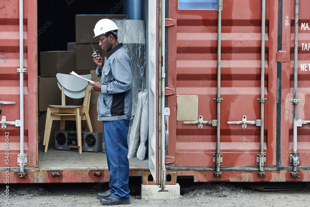 Graphic side view portrait of young male worker wearing hardhat while checking containers at shipping dock, copy space