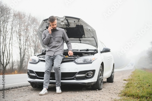 Man use a cellphone call garage in front of the open hood of a broken car on the road in the forest. Car breakdown concept.