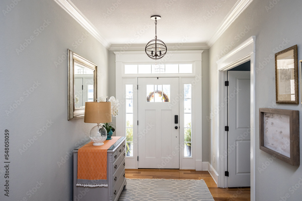An open large and wide interior front door hallway foyer with transom, hanging light fixture, coastal colors and entry way table and wood floors - obrazy, fototapety, plakaty 