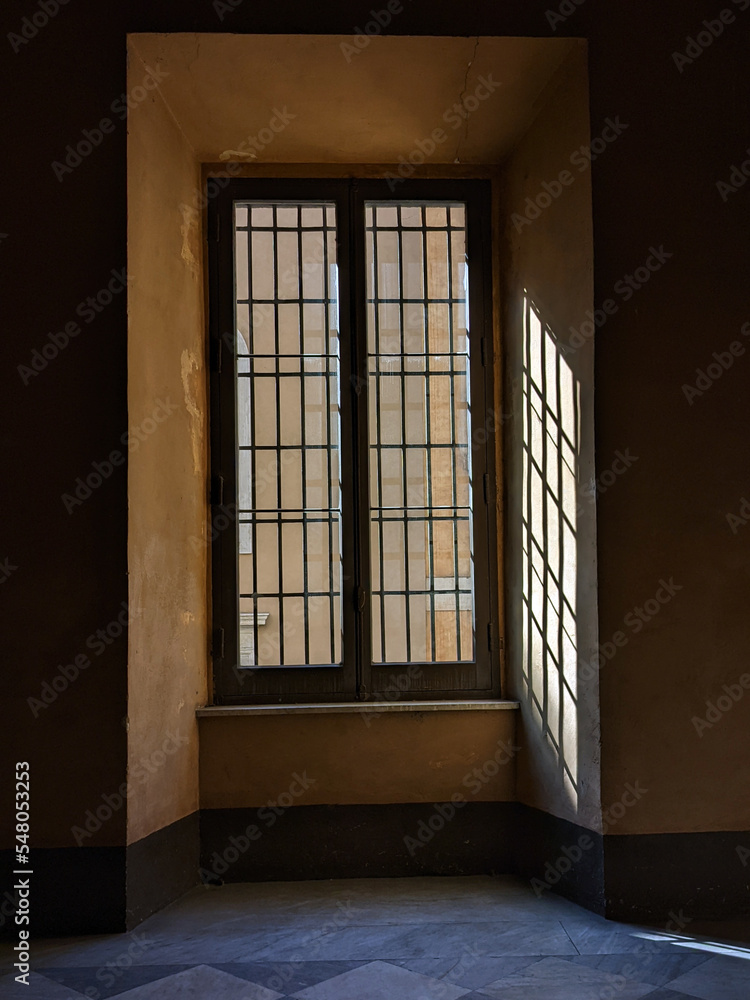 An old window embedded in the wall with the geometric pattern of the lights and shadows of the sun's rays An old window embedded in the wall with the geometric pattern of the lights and shadows of the sun's rays