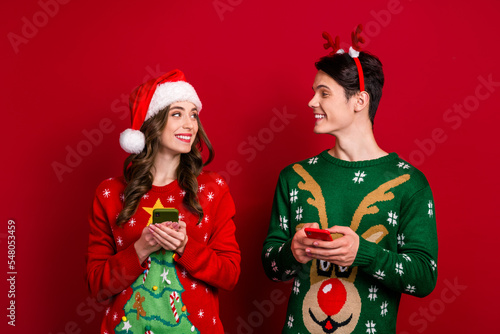 Photo of two positive funny people toothy smile look each other use telephone isolated on red color background