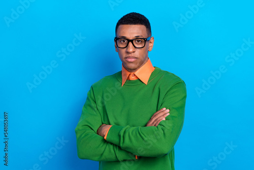 Portrait of confident handsome clever guy wear orange shirt under green pullover eyewear arms folded isolated on blue color background