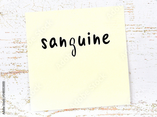 Yellow sticky note on wooden wall with handwritten word sanguine photo
