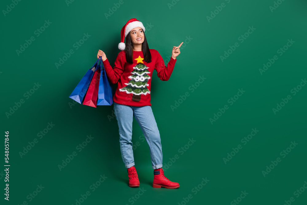 Full length photo of dreamy sweet lady wear red ugly print xmas sweater rising shoppers pointing empty space isolated green color background